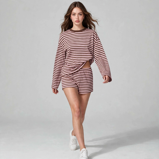 Woman walking in a burgundy and cream striped long-sleeve crop top and shorts set with white sneakers, gray studio.