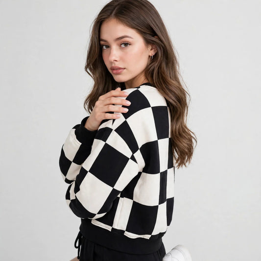 Close-up of model in black and white checkerboard sweatshirt, ribbed cuffs, three-quarter view, light grey studio backdrop.