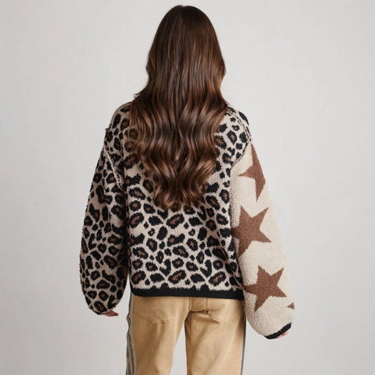 Back view of a woman in a cream knit sweater with leopard back panel and brown stars, tan pants, gray studio backdrop.