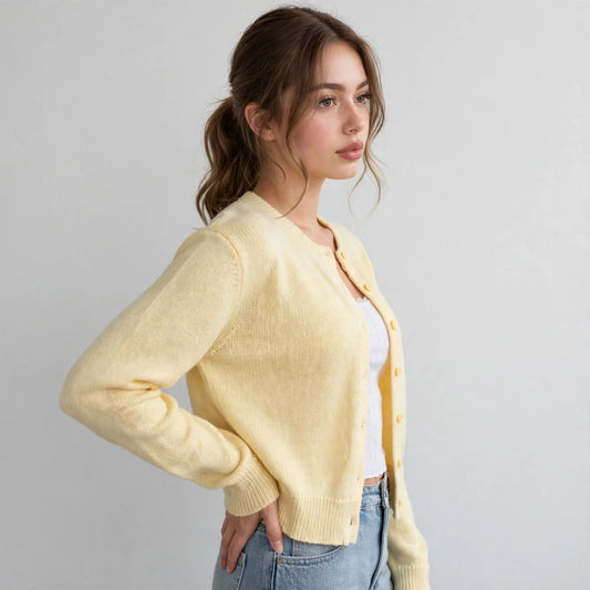 Side view of model with hand on hip wearing a pale yellow button-up knit cardigan with long sleeves and blue jeans