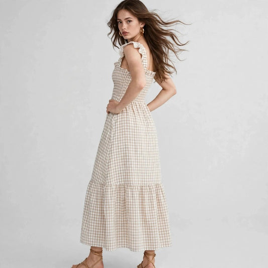 Model in beige gingham plaid maxi dress with ruffle sleeves, smocked bodice, three-quarter side view, studio backdrop.