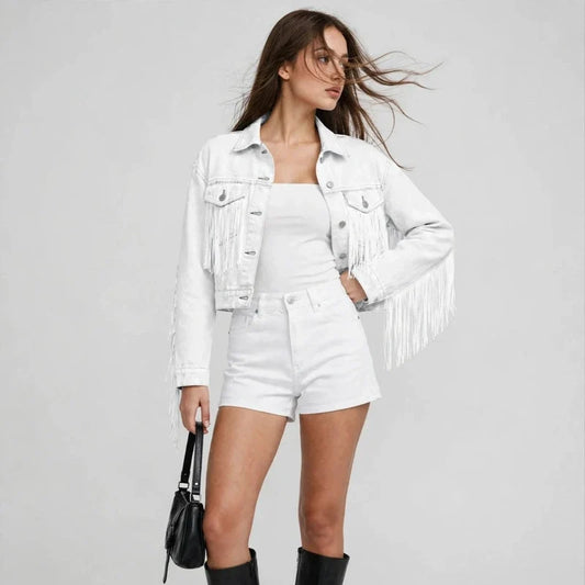 Front view of a woman wearing a white fringed cropped denim jacket with white shorts, black boots, and a handbag.