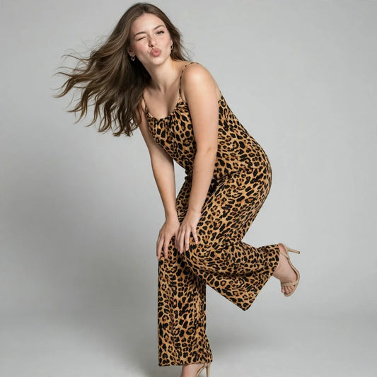 Woman winking at the camera wearing a leopard print scoop-neck wide-leg jumpsuit, hair flowing, gray studio background.