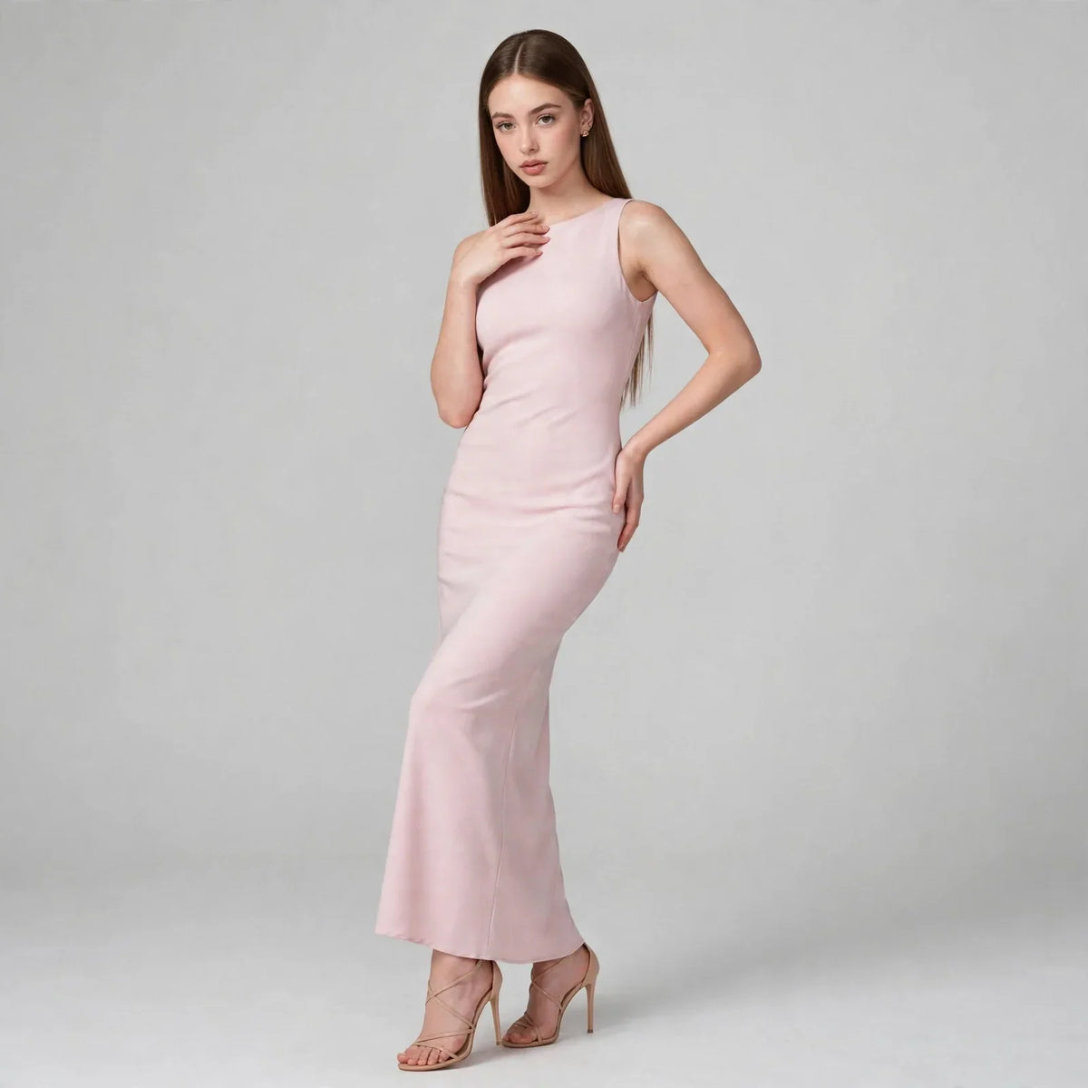 Woman in a light pink sleeveless satin maxi dress with high neckline, hand at neck, front view, gray studio background.