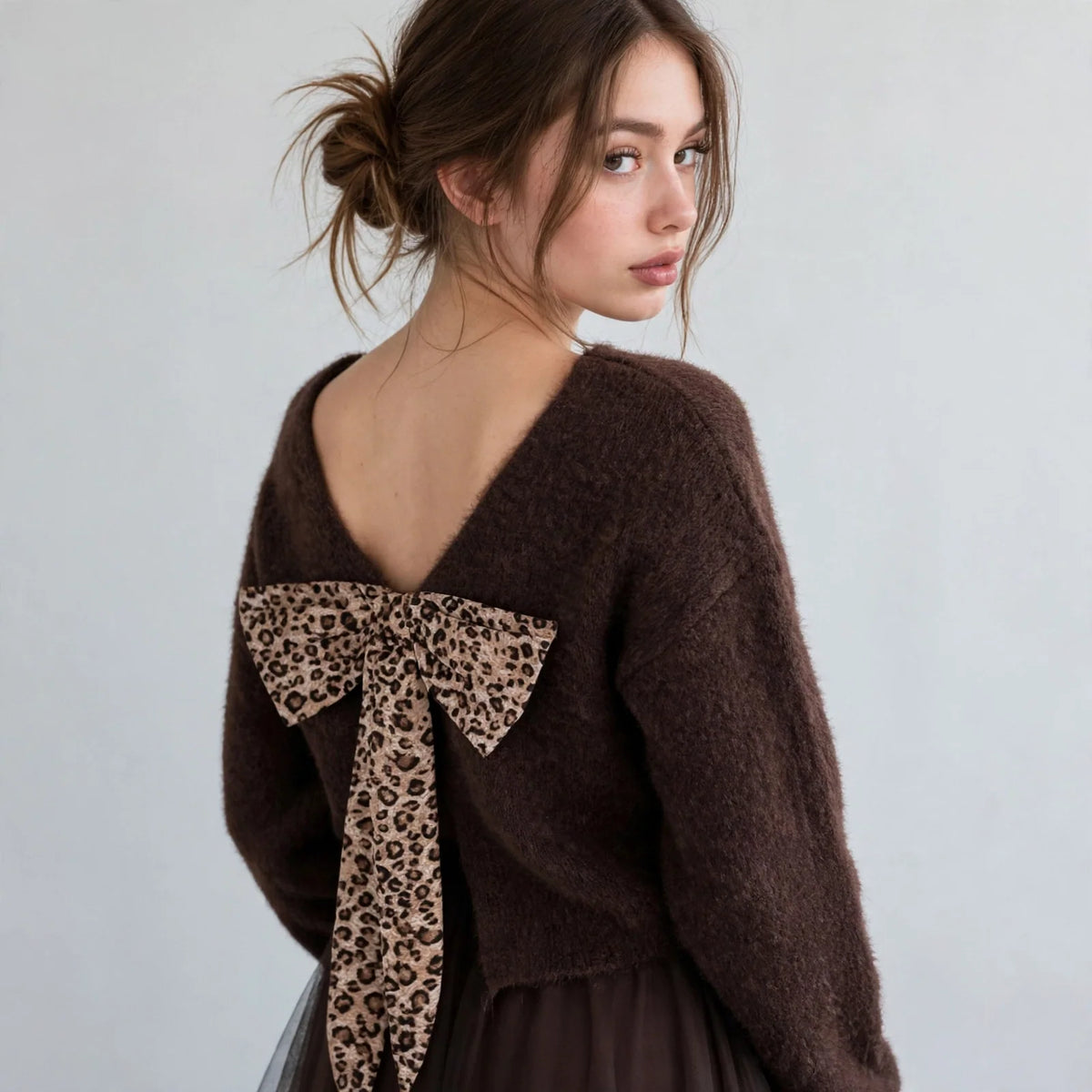 Back view of brown fuzzy dropped-shoulder sweater with leopard-print bow at open back neckline on model, studio shot.