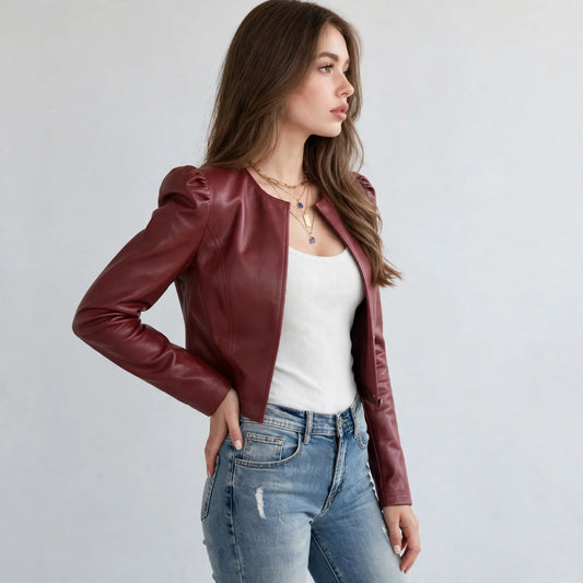 Side view of a model in a burgundy faux leather puff-sleeve jacket, hand on hip, white top and jeans, gray background.