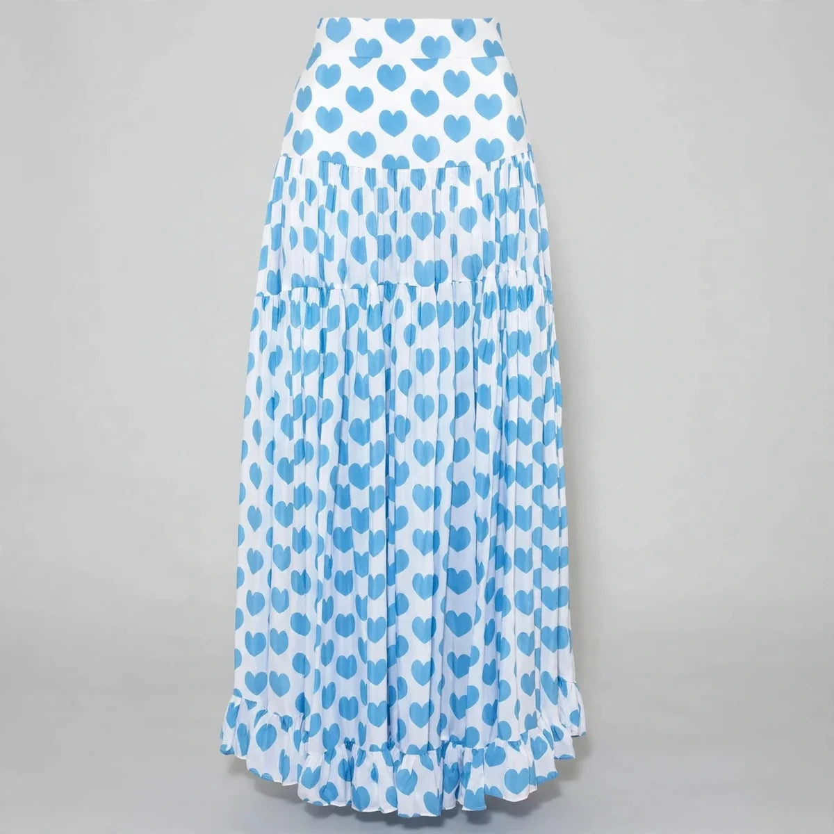Flat lay of a blue heart-print pleated maxi skirt with tiered ruffled hem on a neutral gray background.
