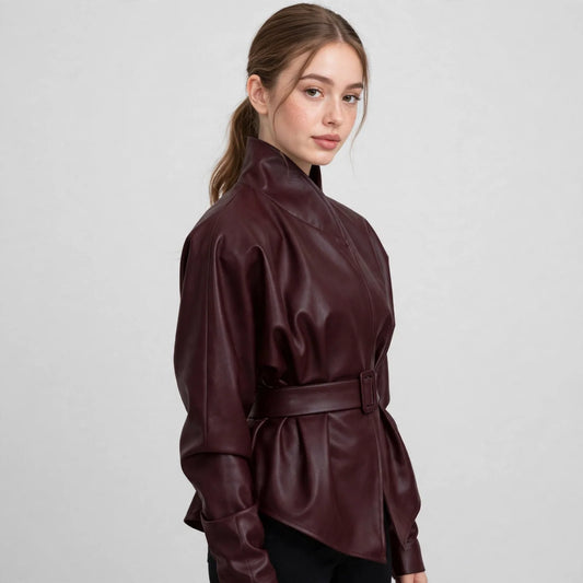 Side view of a woman wearing a burgundy belted faux leather jacket with stand collar and black pants, gray studio background.
