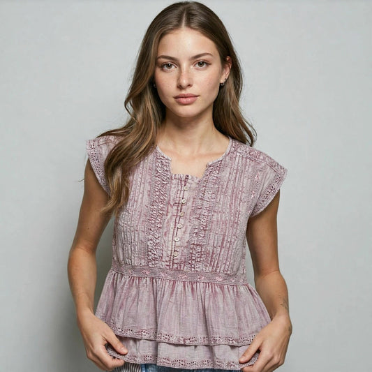 Woman modeling a dusty mauve sleeveless peplum top with vertical pintuck stripes against a light gray studio background.