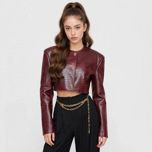 Woman in a burgundy crocodile-embossed cropped leather jacket with black pants and gold chain, front view, gray background.