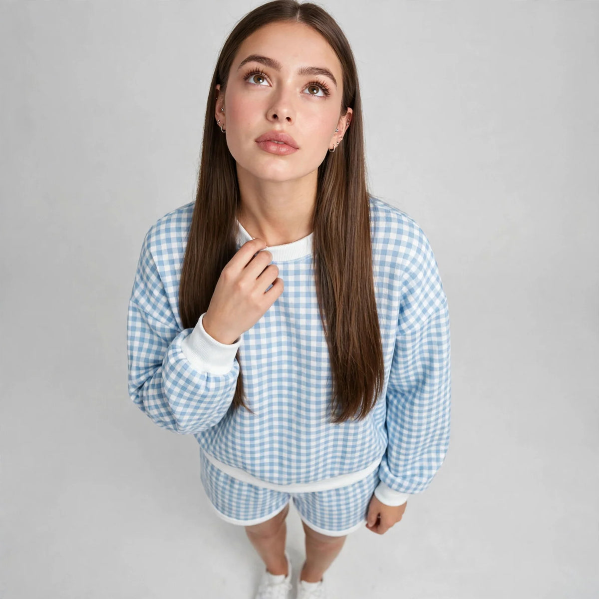 High-angle close-up of a blue and white gingham sweatshirt showing the check pattern and white ribbed neckline, model view.