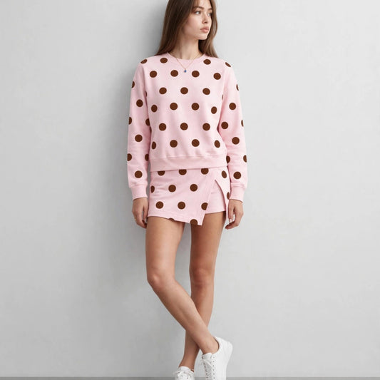 Front view of a woman in a light pink long-sleeve sweatshirt and matching shorts with brown polka dots, white sneakers.