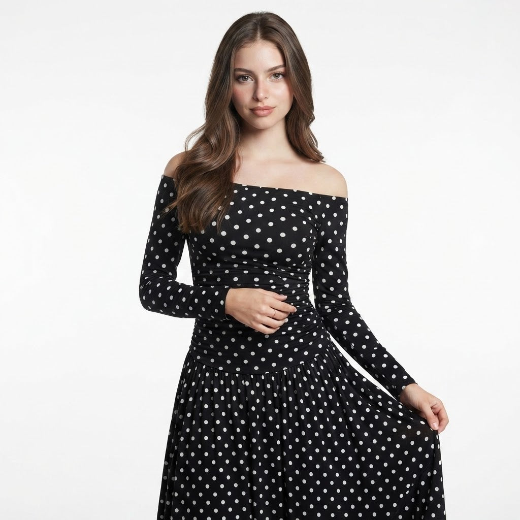 Woman in a black off-the-shoulder long-sleeve maxi dress with white polka dots and ruched bodice, white studio background.