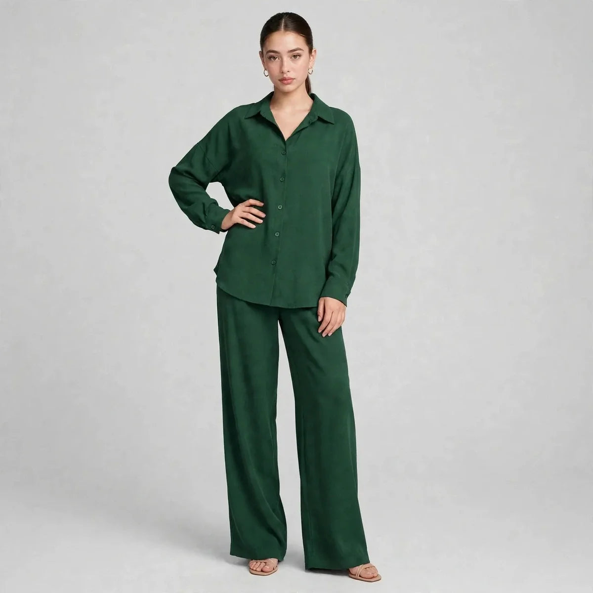 Woman modeling a dark green two-piece set with long-sleeve button-up shirt and matching wide-leg pants, gray background.