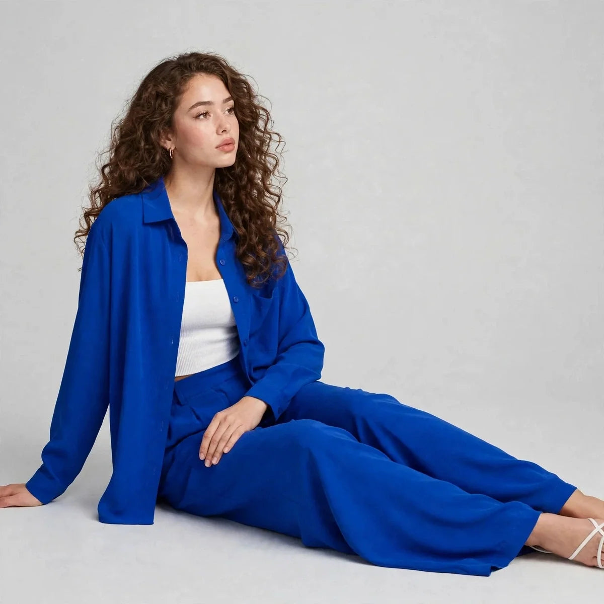 Woman sitting on the floor wearing a royal blue button-up shirt and wide-leg pants set layered over a white bandeau top.
