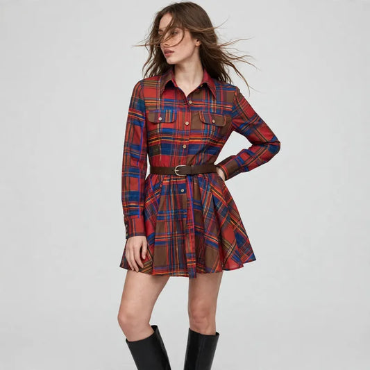 Woman standing in a red plaid long-sleeve shirt dress with collar, chest pockets and belt, black boots, gray studio.