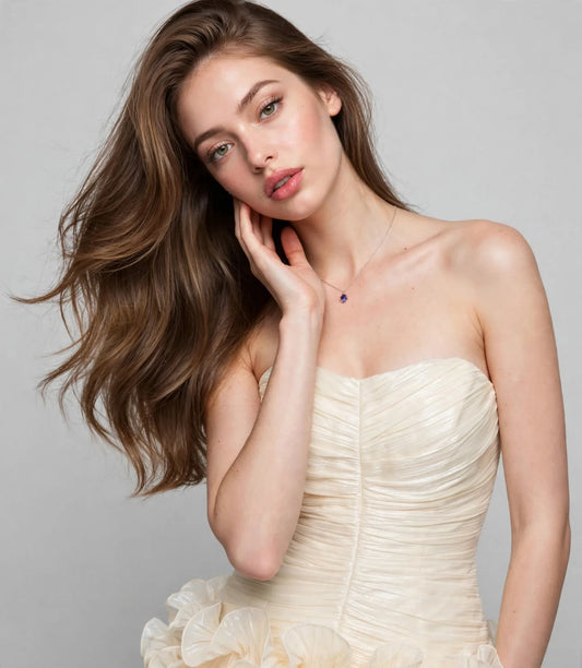Close-up portrait of a woman wearing a cream strapless mini dress with a ruched pleated bodice and a delicate necklace.