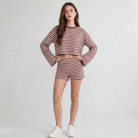 Woman in a brown and white striped long-sleeve crop top and shorts set with white sneakers, hands on waist, gray studio.