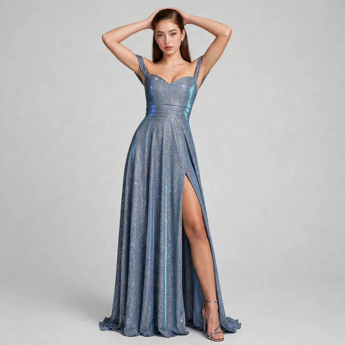 Woman in a shimmering blue-gray gown with sweetheart neckline, thin straps and high thigh slit, gray studio background.