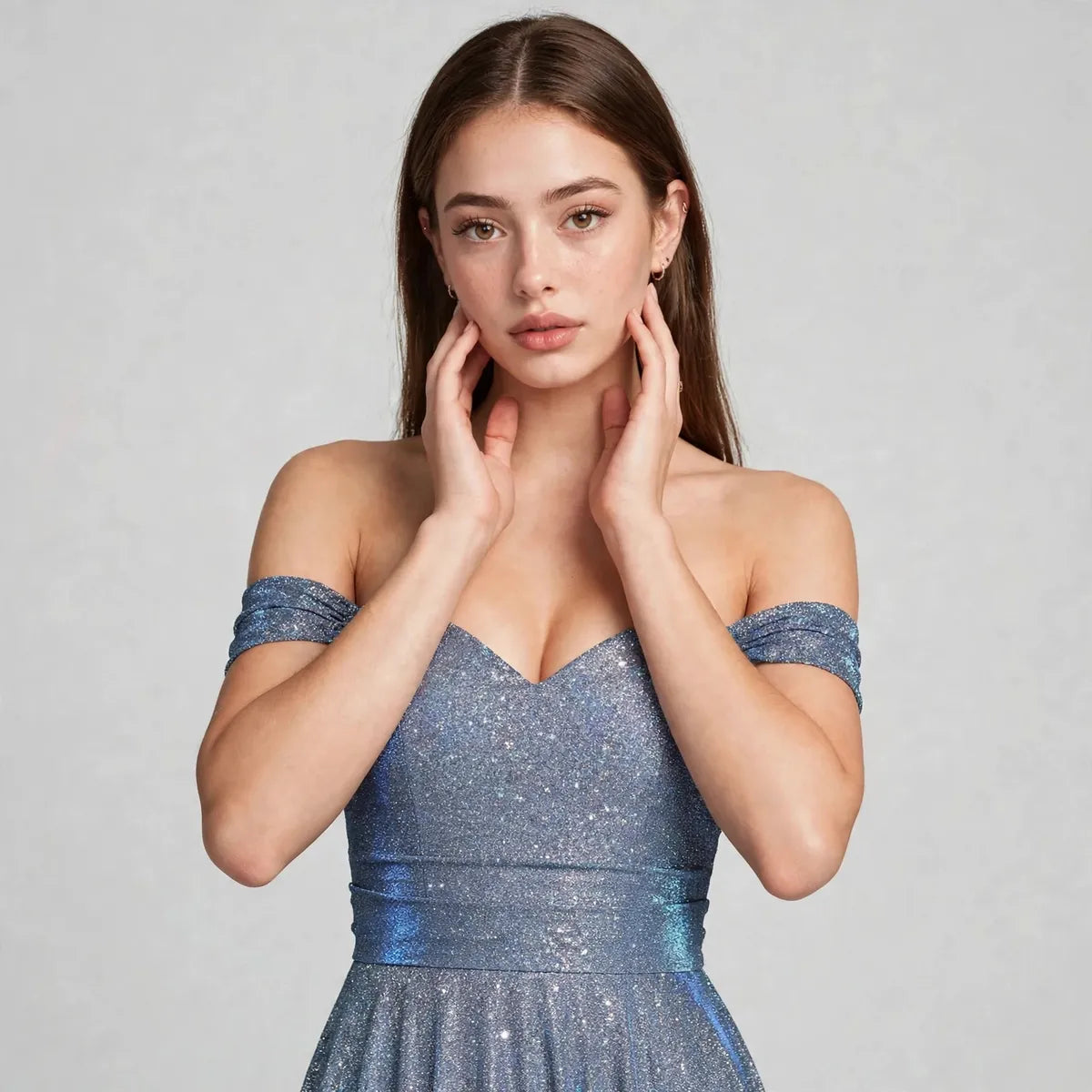 Close-up of an off-the-shoulder sparkly blue dress worn by a woman, hands near face, gray studio background.