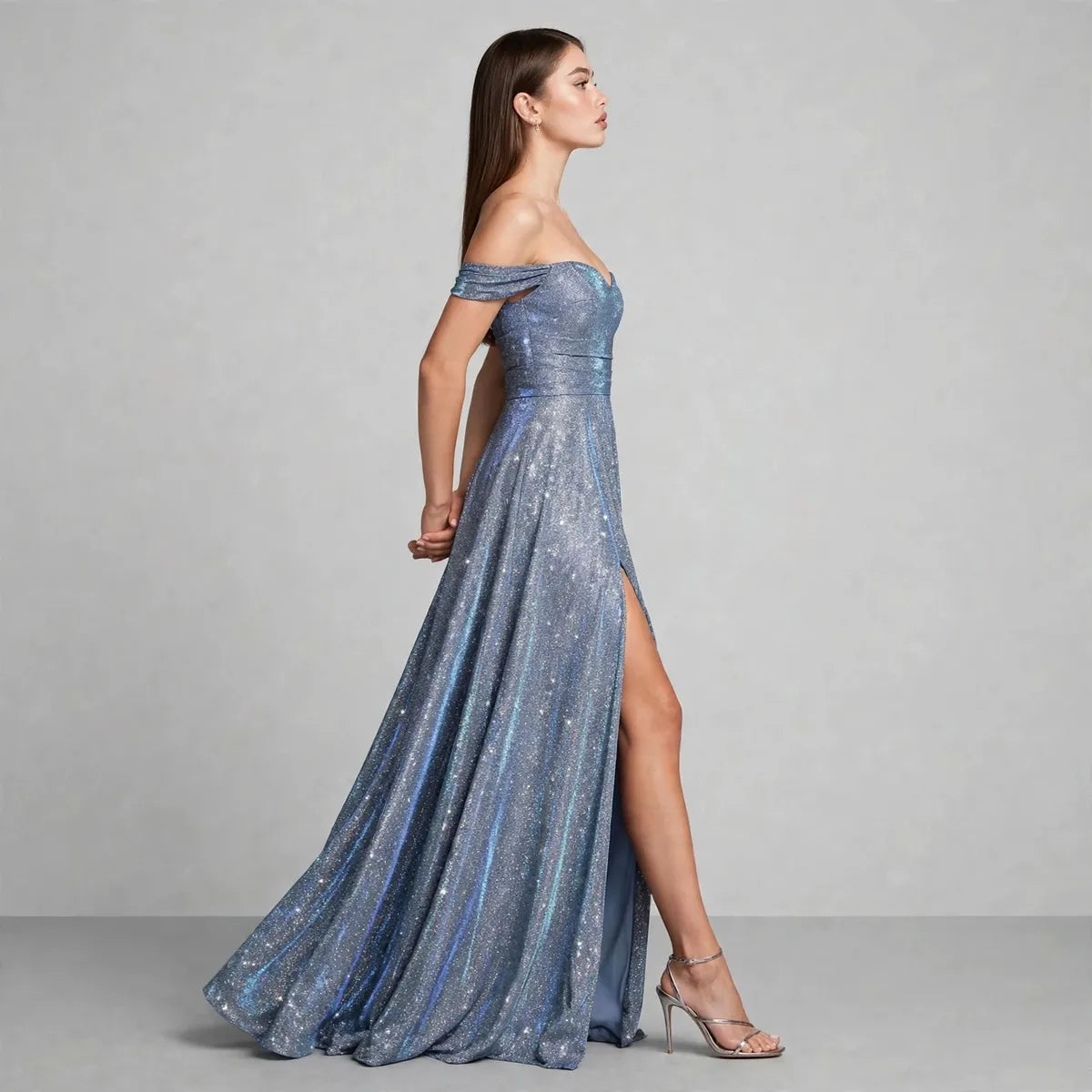 Side view of an off-the-shoulder blue gown with thigh-high slit and shimmering sequin texture, gray studio background.
