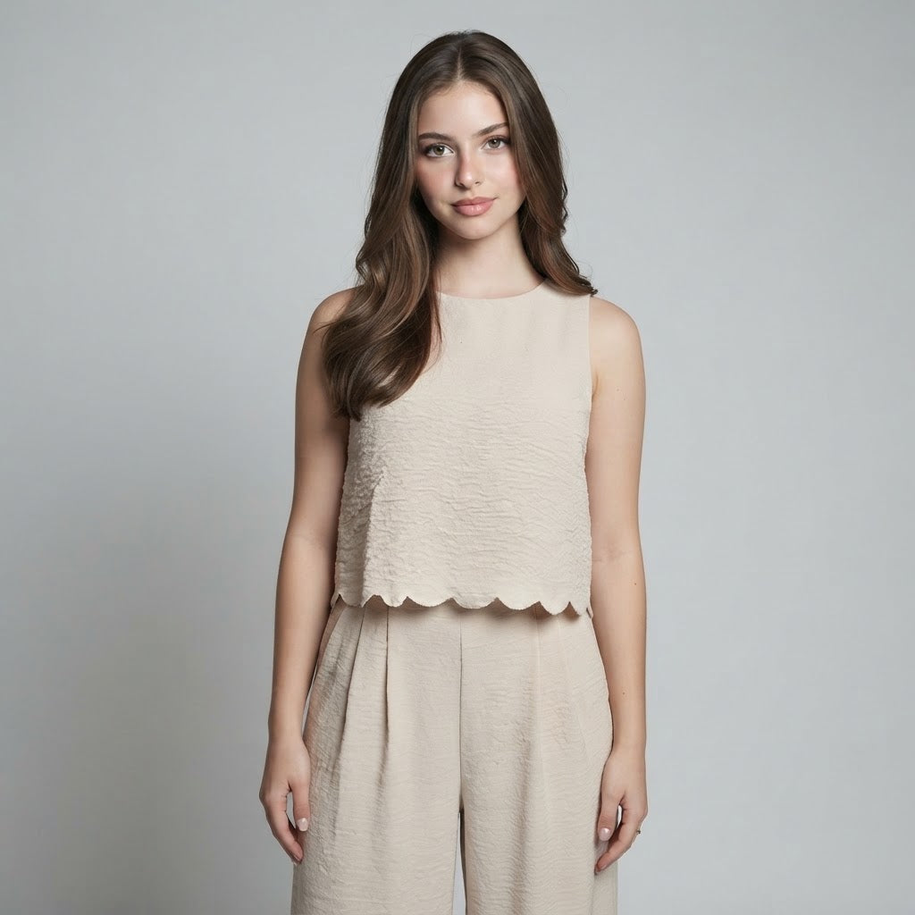 Woman modeling a beige sleeveless textured top with scalloped hem and matching wide-leg pants on a gray studio background.