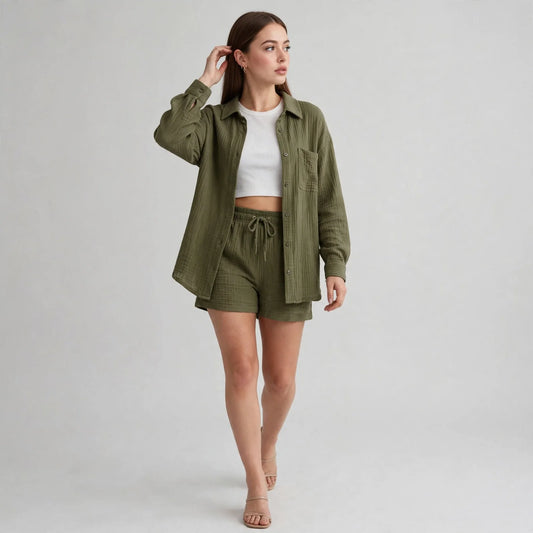 Woman in an olive green button-up shirt and shorts over a white crop top, beige heeled sandals, gray studio background.