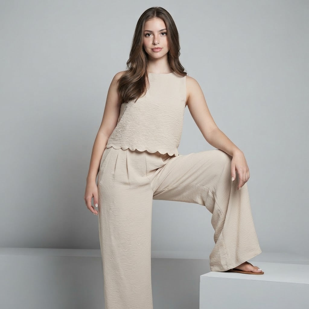 Woman posing with one leg raised wearing a beige sleeveless textured top with scalloped hem and matching wide-leg pants.