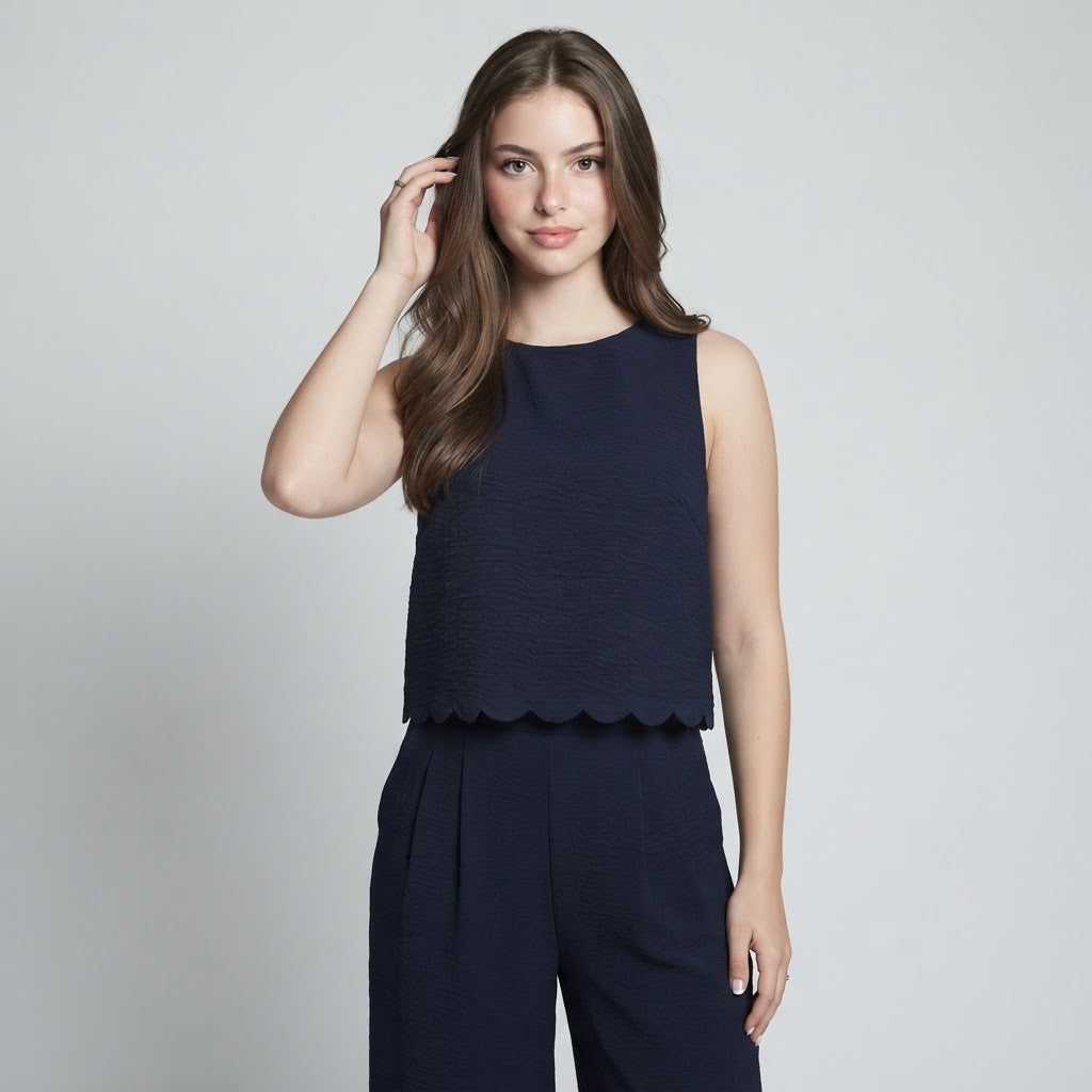 Woman modeling a navy sleeveless textured top with scalloped hem and matching navy wide-leg pants, gray studio background.