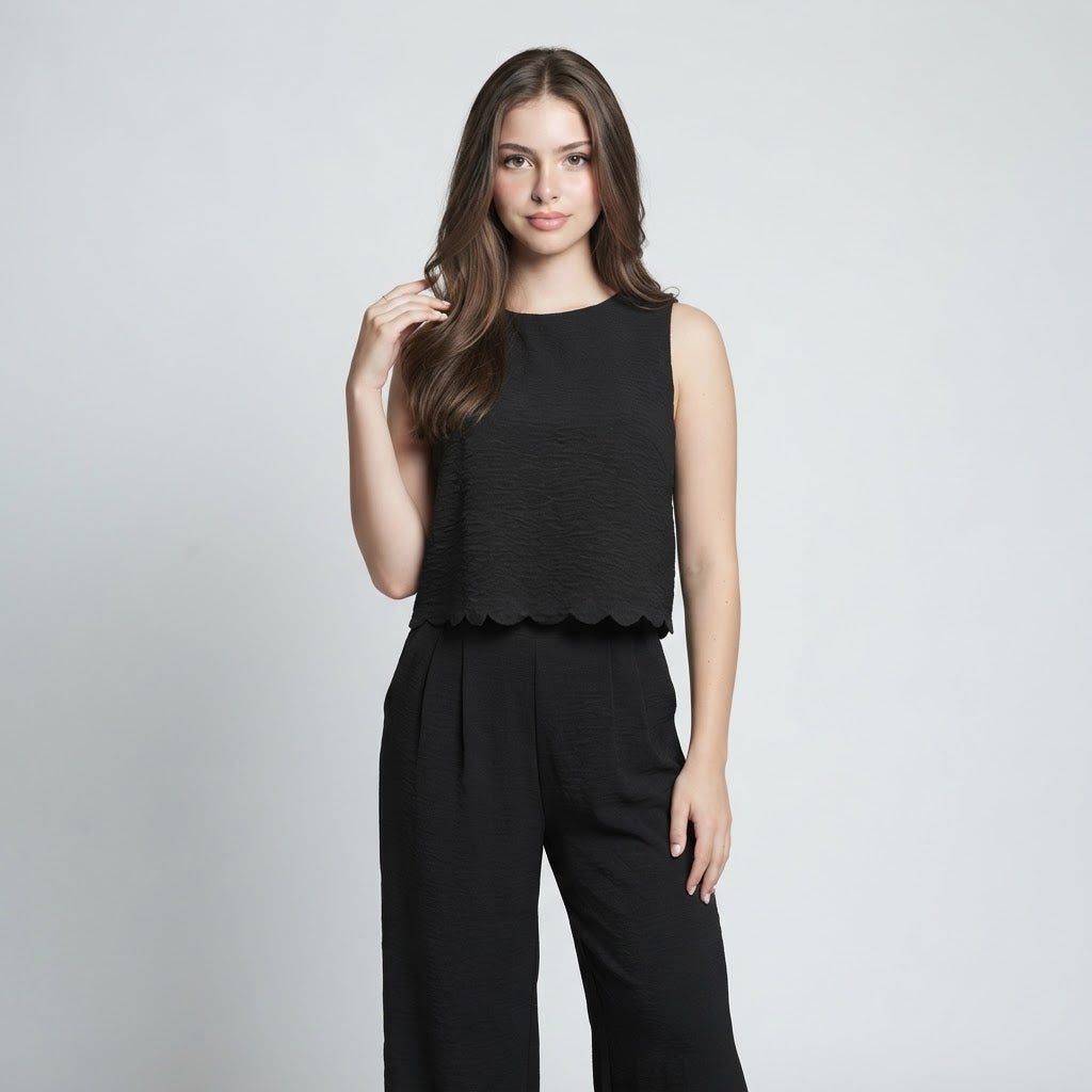 Woman modeling a black sleeveless textured top with scalloped hem and matching black wide-leg pants, gray studio background.