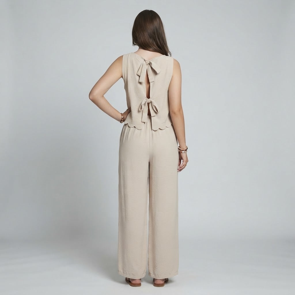 Back view of a woman wearing a beige sleeveless top with bow tie-back detail and matching wide-leg pants, gray background.