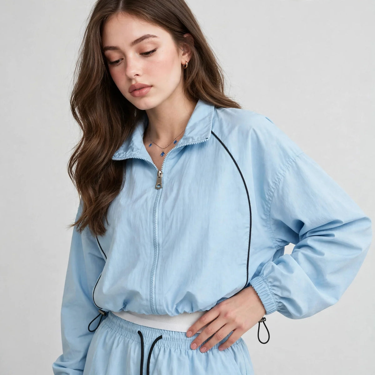 Close-up of a light blue zip-up windbreaker with collar and black piping, upper-body view, light gray studio background.