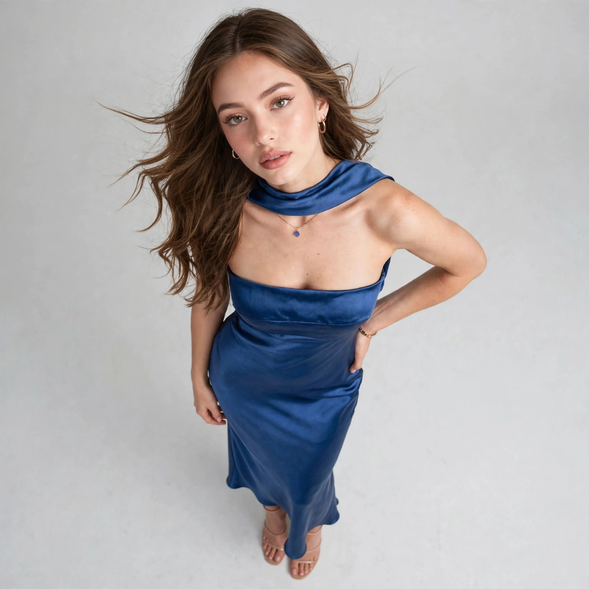 High-angle close-up of a blue satin tube maxi dress neckline with draped choker detail, model looking up, white background.