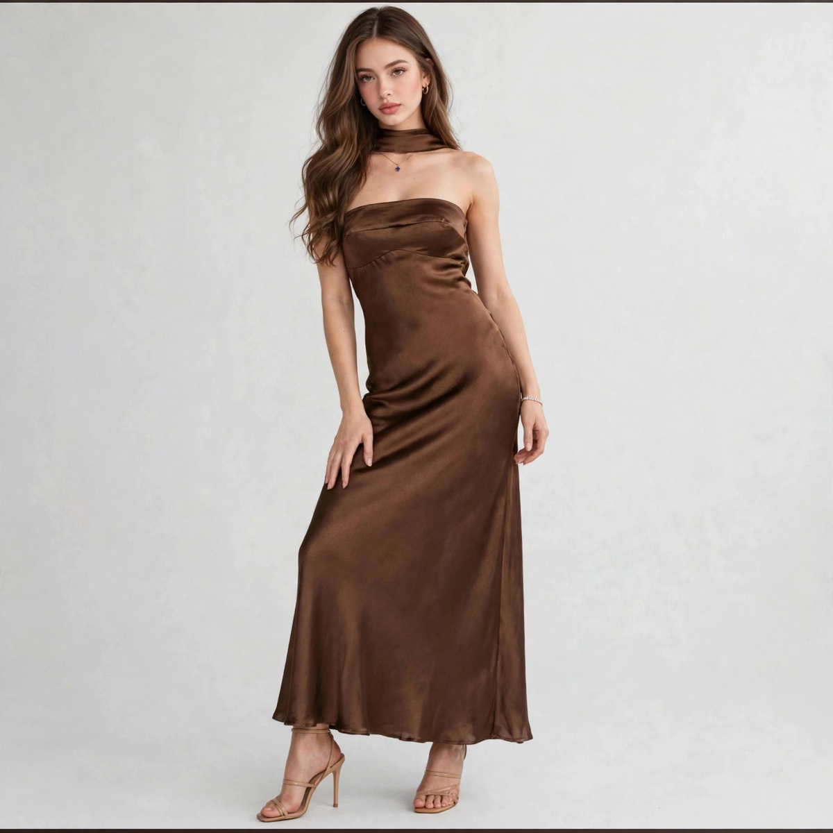 Model walking toward camera in a brown satin tube maxi dress with draped choker neckline, white studio background.