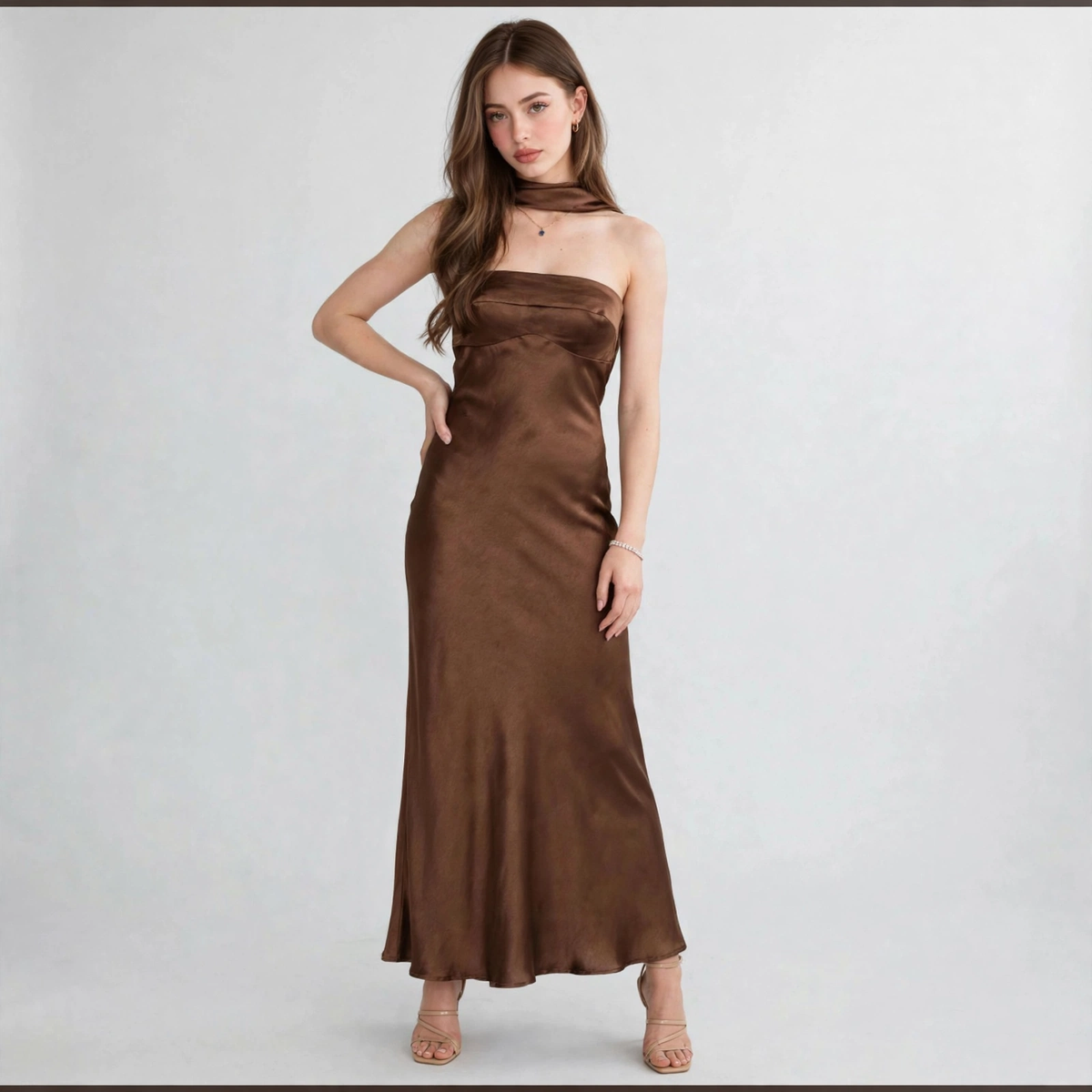 Model in a brown satin tube maxi dress with draped choker neckline, hand on hip pose, white studio background.