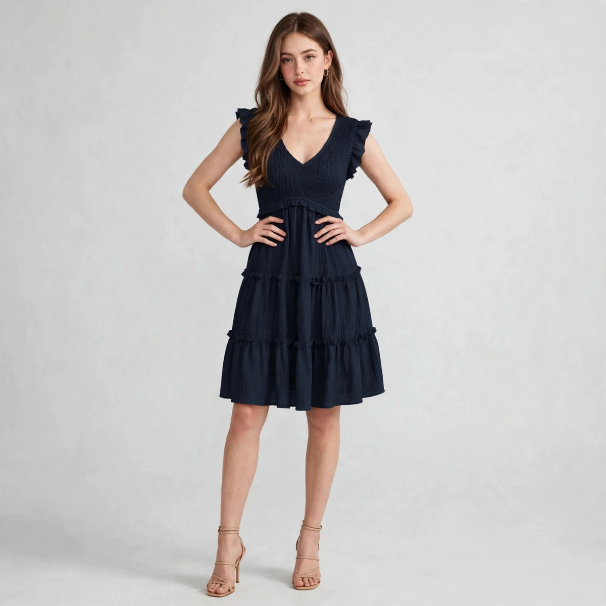 Model in navy ruffled V-neck cap sleeve mini dress with smocked bodice and tiered ruffle skirt, front view, studio backdrop.