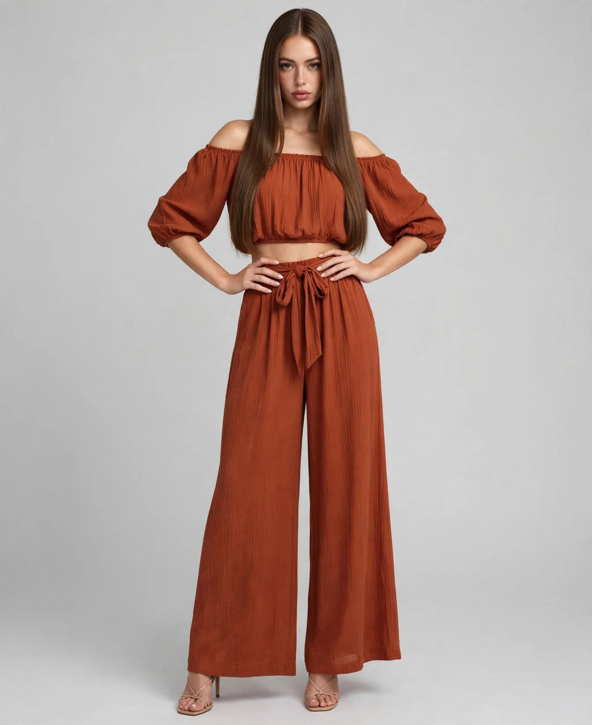 A rust off-shoulder two-piece set with cropped top, 3/4 puff sleeves and tie-waist wide-leg pants, grey backdrop.