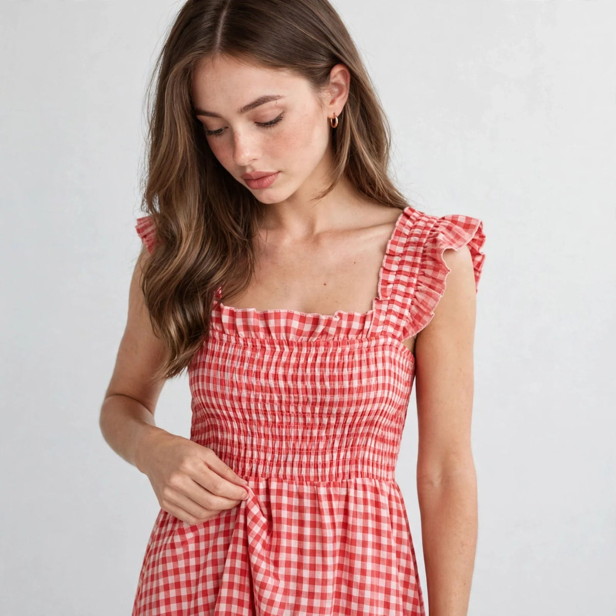Close-up of red gingham plaid maxi dress neckline with ruffle cap sleeves and smocked bodice detail on model, studio shot.