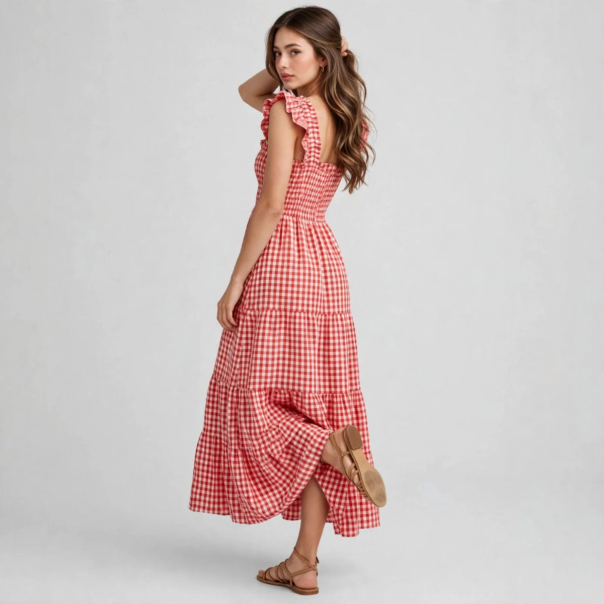 Model in red gingham plaid maxi dress with ruffle cap sleeves and smocked back, three-quarter back view, studio backdrop.