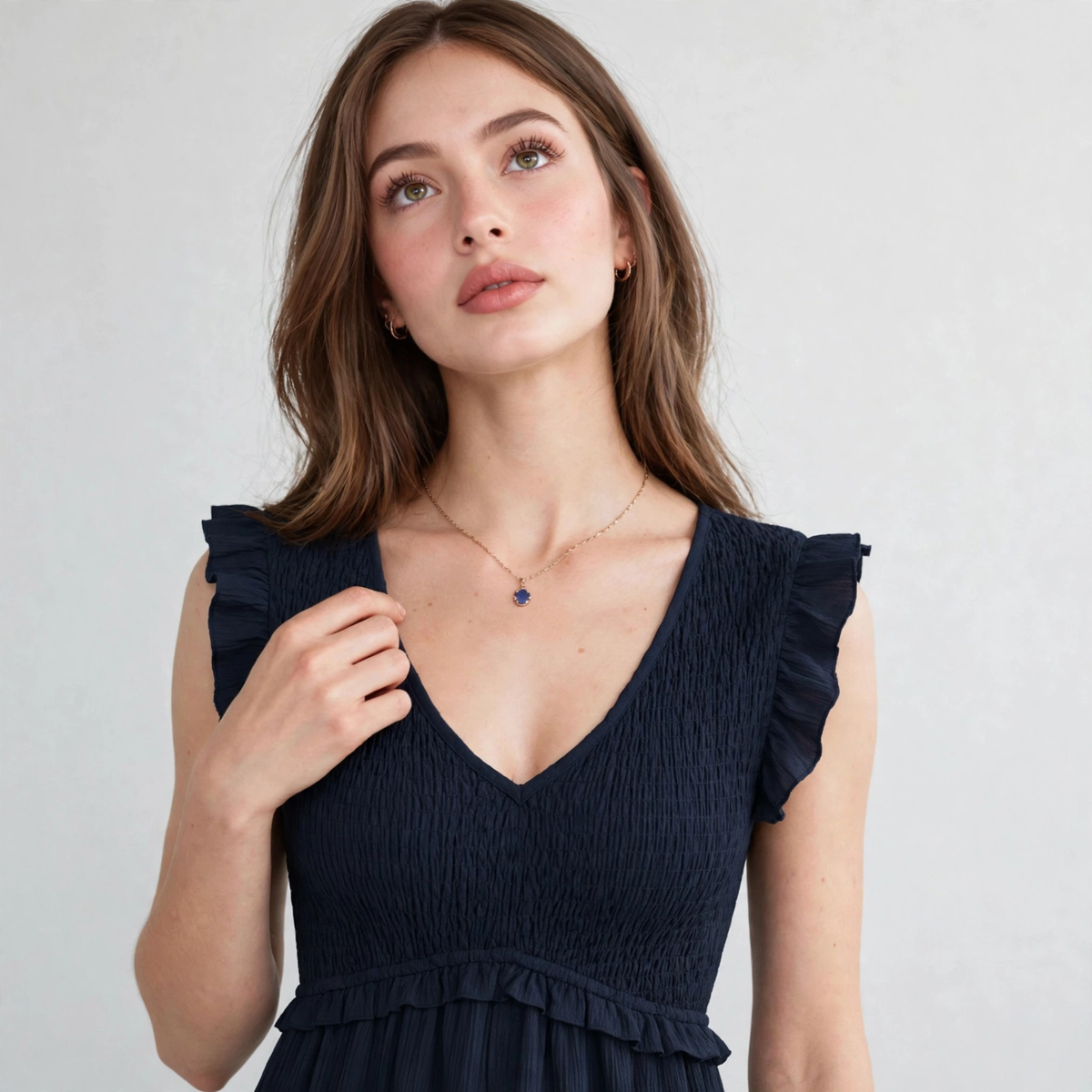 Close-up of navy ruffled V-neck cap sleeve dress showing ruffle shoulder detail, smocked bodice and delicate necklace, model.