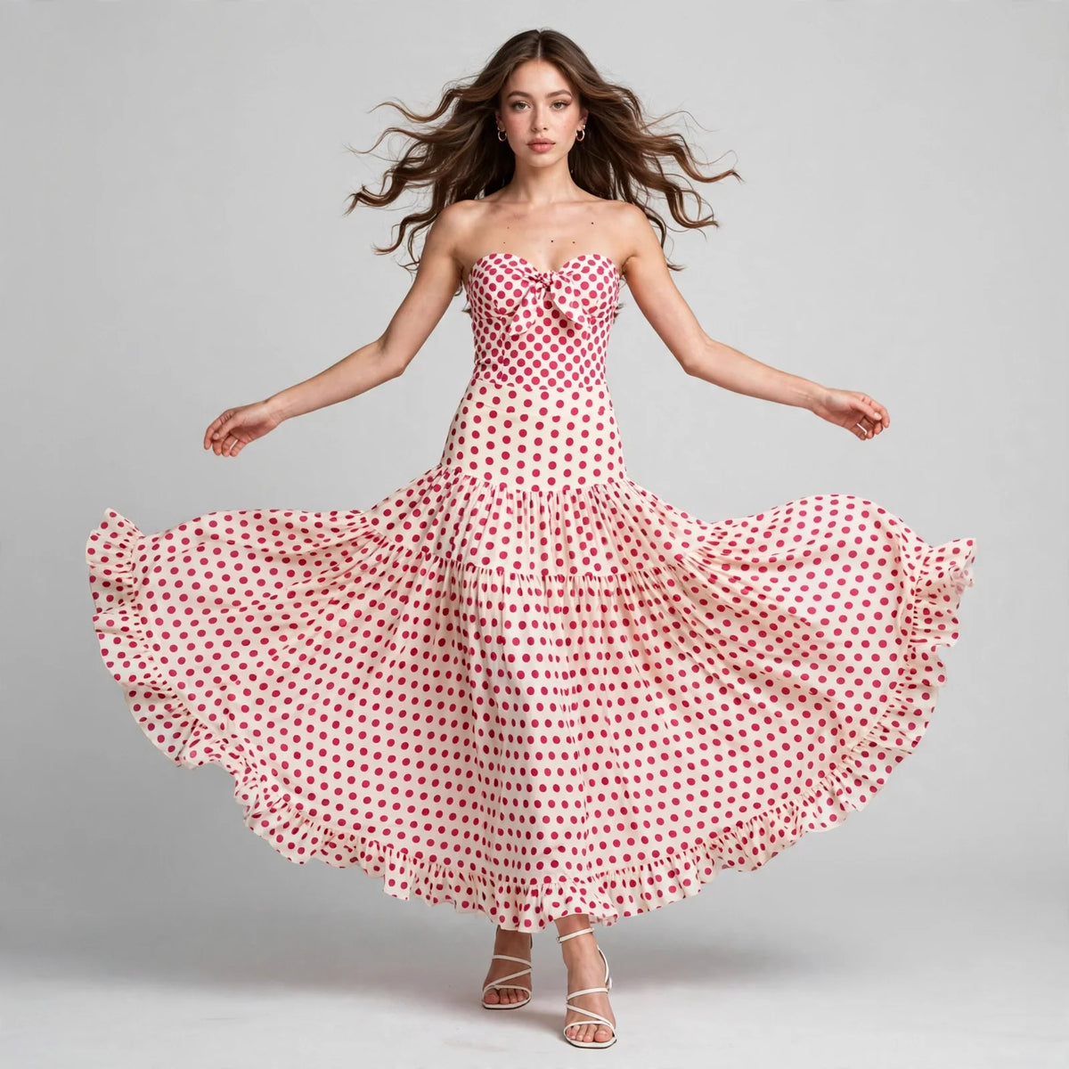 Model twirling in a red heart-print strapless swimsuit and tiered maxi skirt set with ruffled hem, gray studio.