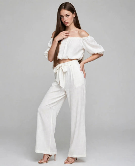A white off-shoulder two-piece set with cropped puff-sleeve top and tie-waist wide-leg pants, grey studio backdrop.
