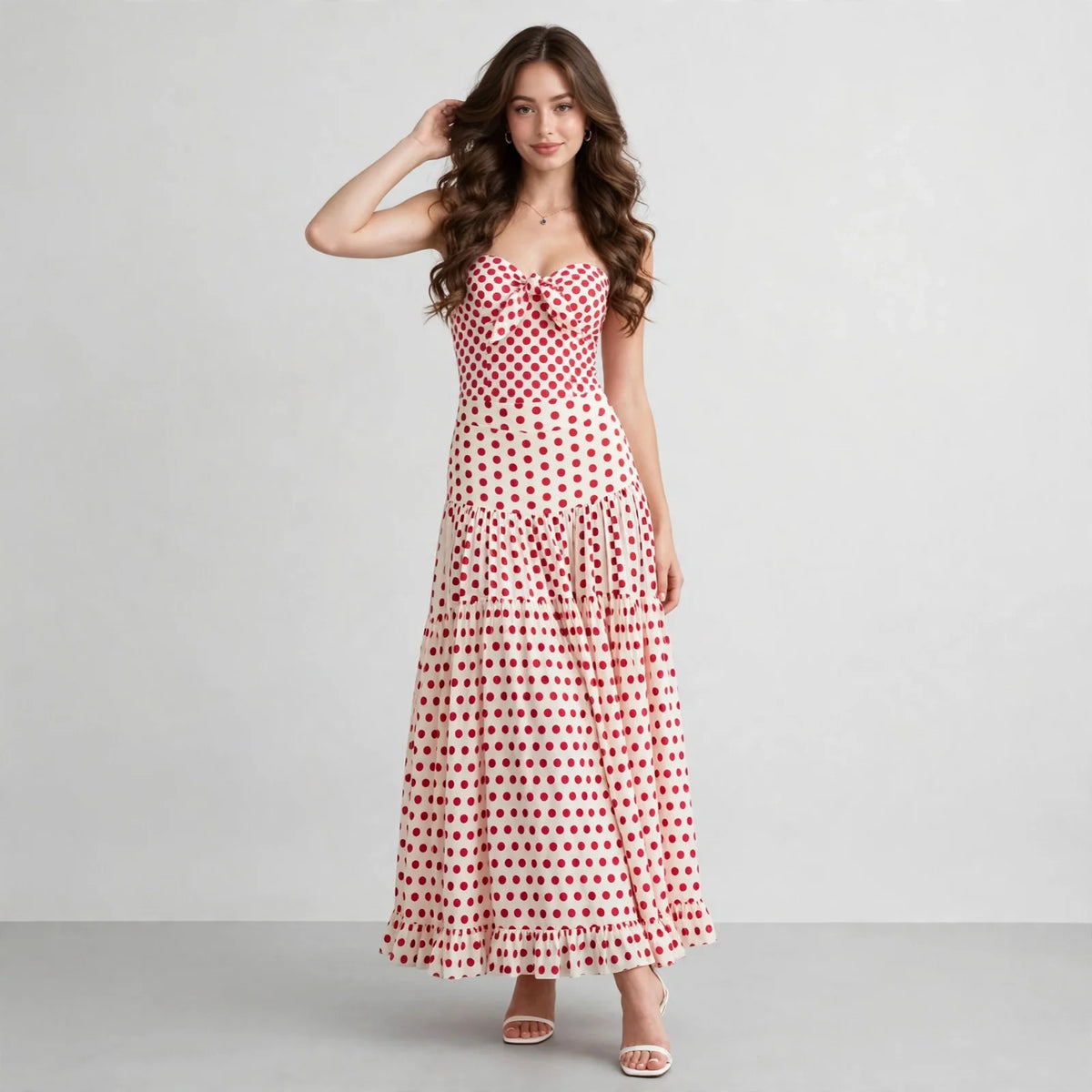 Front view of a red heart-print strapless swimsuit and tiered maxi skirt set, model with hand in hair, gray studio.