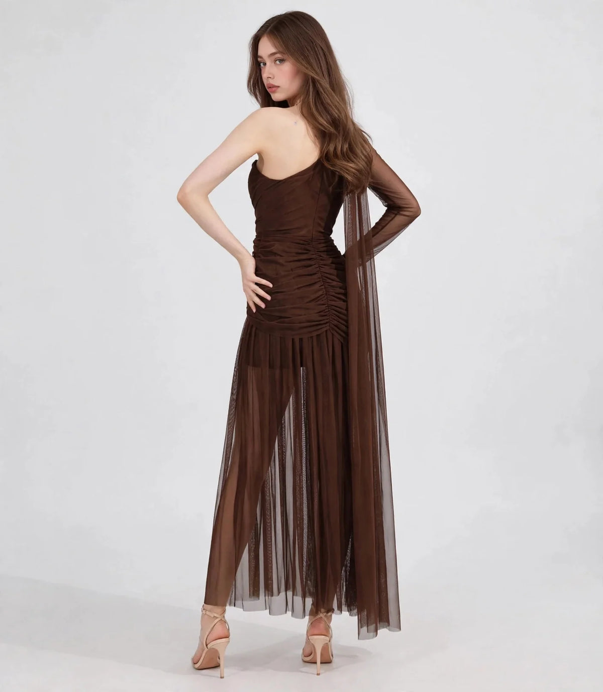 Back view of model in brown one-shoulder mesh dress with sheer back drape and flowing skirt, white background