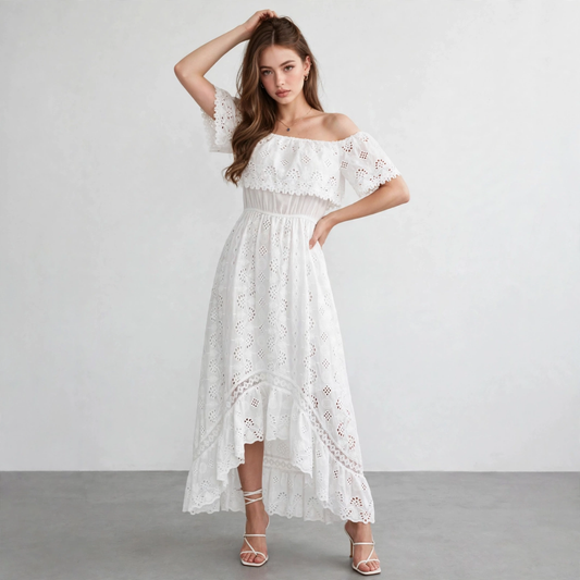 Full-length view of a model in a white off-shoulder eyelet maxi dress with high-low hem, hand raised, gray studio backdrop.