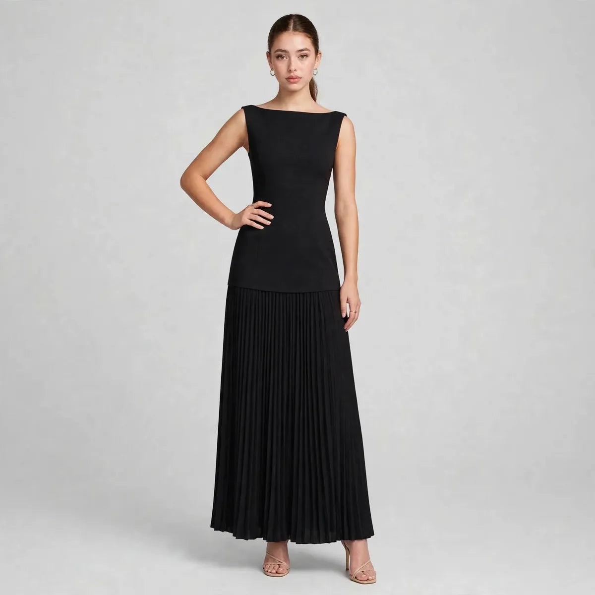 Front view of a black sleeveless pleated maxi dress with fitted bodice and flowing skirt, model posing in studio.