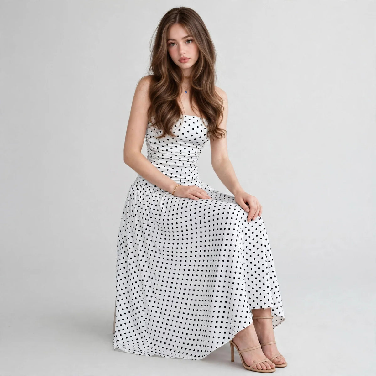 Front view of a white polka dot strapless maxi dress with flared flowy skirt and smocked bodice, white studio background.