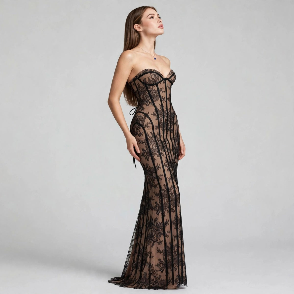 Side view of model in black lace strapless maxi dress with corset-style bodice and sheer lace overlay, studio backdrop.