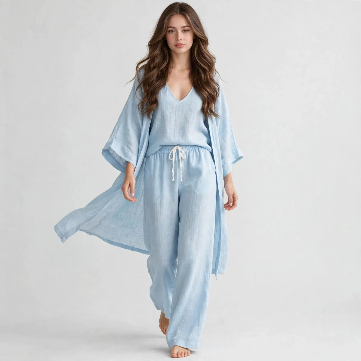 Woman in a light blue V-neck top, open cardigan and drawstring pants set, walking pose, light gray studio background.