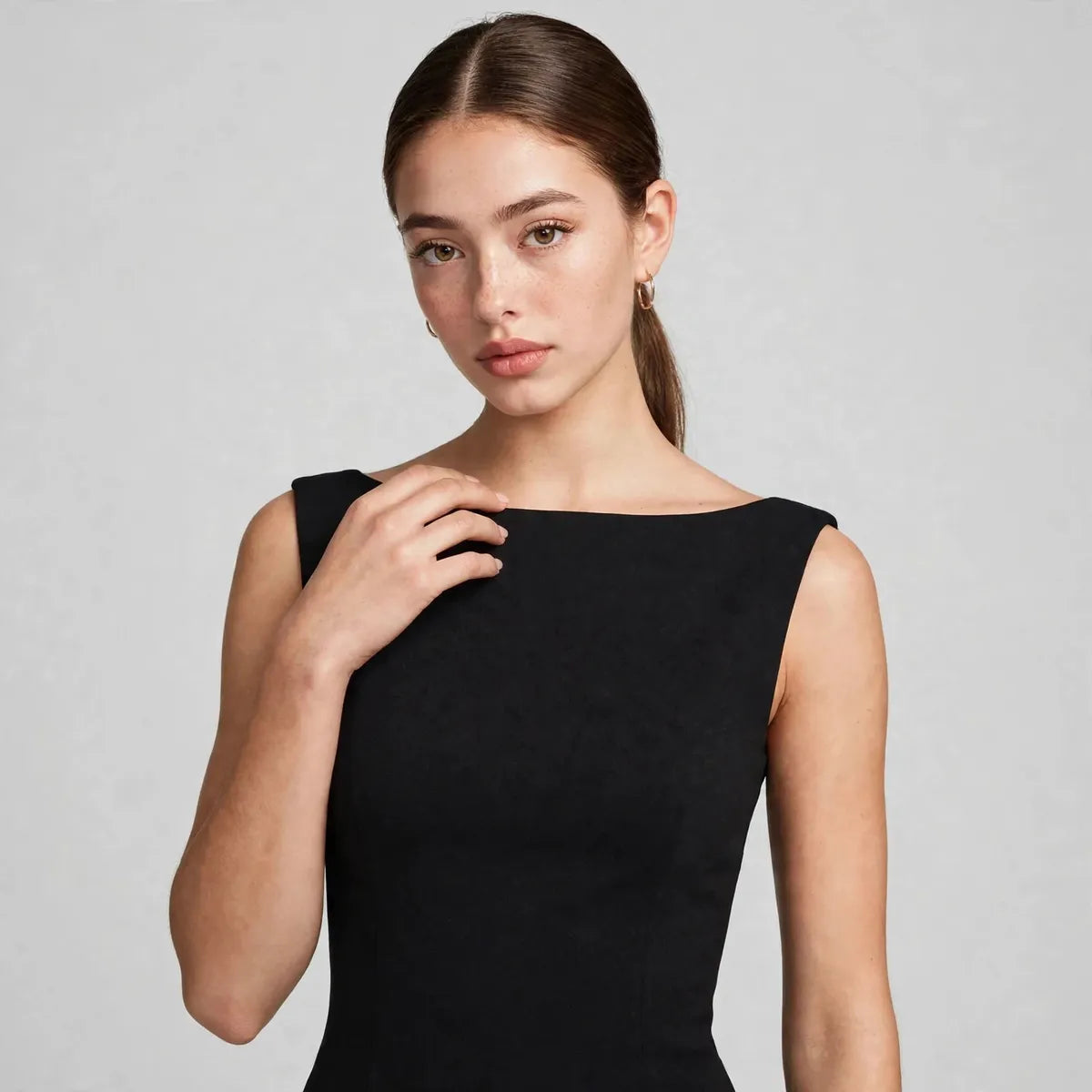 Close-up portrait showing the boat neckline and fitted bodice of a black sleeveless maxi dress, gray background.